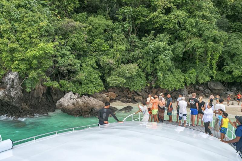 Tourists on a boat trip in Phi Phi Island with clear waters and limestone cliffs.