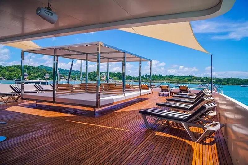 A large open lounge area on a luxury yacht with sunbeds and shades, offering a stunning view of the 
