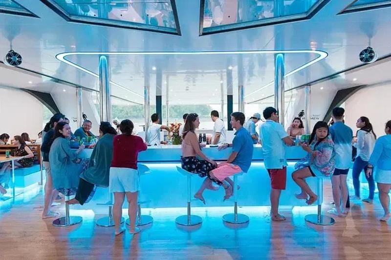 A modern bar area on a yacht with guests socializing and enjoying drinks under ambient blue lighting