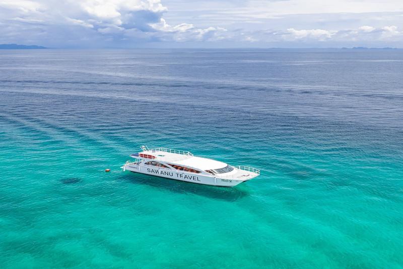 A Sawanu Travel catamaran cruising in the turquoise waters near Phi Phi Bamboo Island, with clear bl