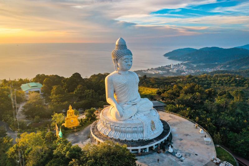 The Big Buddha statue in Phuket, Thailand, illuminated under a bright sky with visitors at the site.