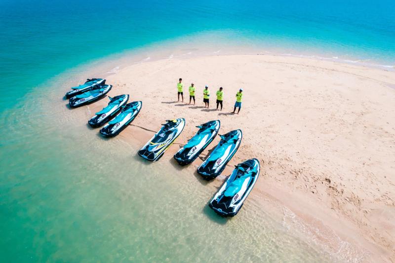 A tropical beach in Phuket with clear turquoise water, soft sand, and lush green trees lining the co