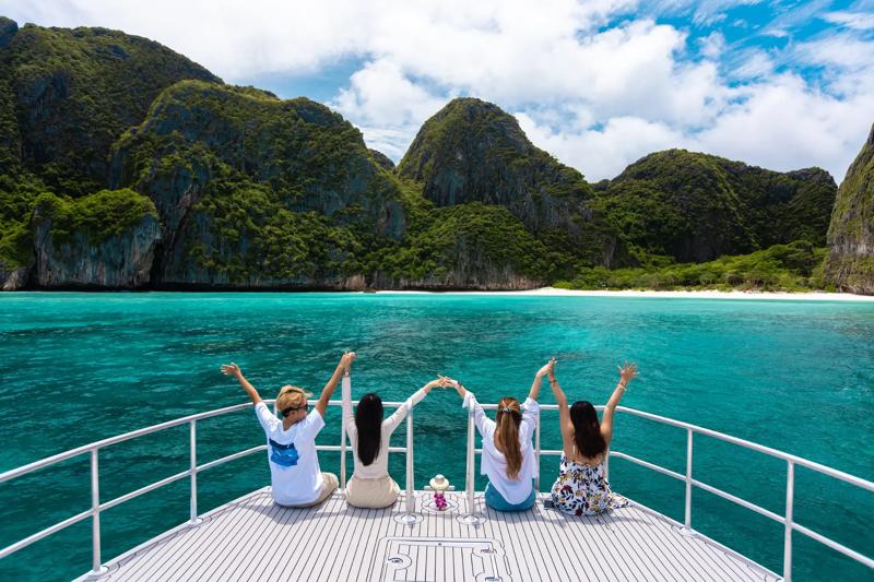 A group of friends enjoying the scenic view from a boat, overlooking clear blue waters and rocky hil
