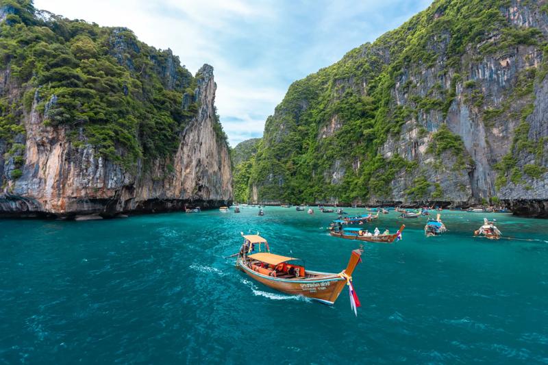 A long-tail boat navigating scenic waters with towering cliffs in Thailand in the background.