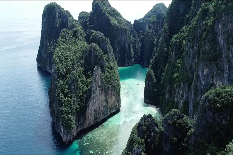 Aerial view of towering tropical cliffs surrounding blue waters in Thailand.